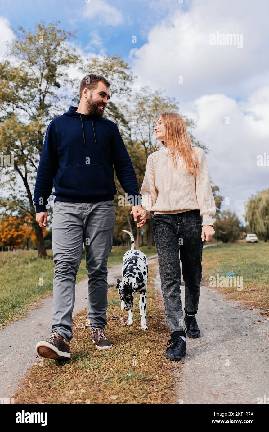 Una bella coppia è a piedi nel parco con il loro cane. Una data per una coppia all'aperto. Foto Stock