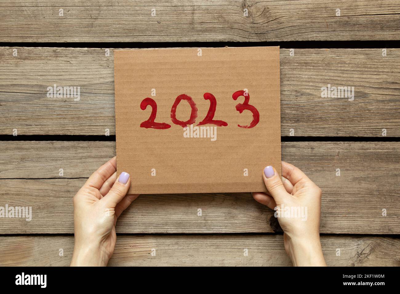 Le mani femminili tengono un poster con il testo 2023 su uno sfondo di legno, felice anno nuovo 2023, l'inizio dell'anno Foto Stock