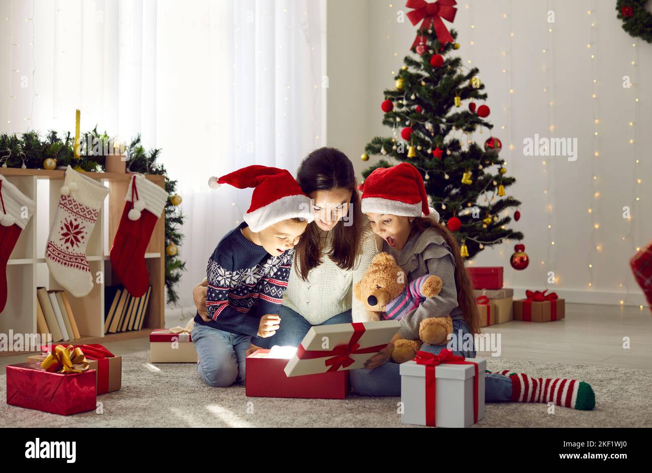 Madre felice e bambini trovano la sorpresa magica mentre aprono i regali di Natale insieme Foto Stock