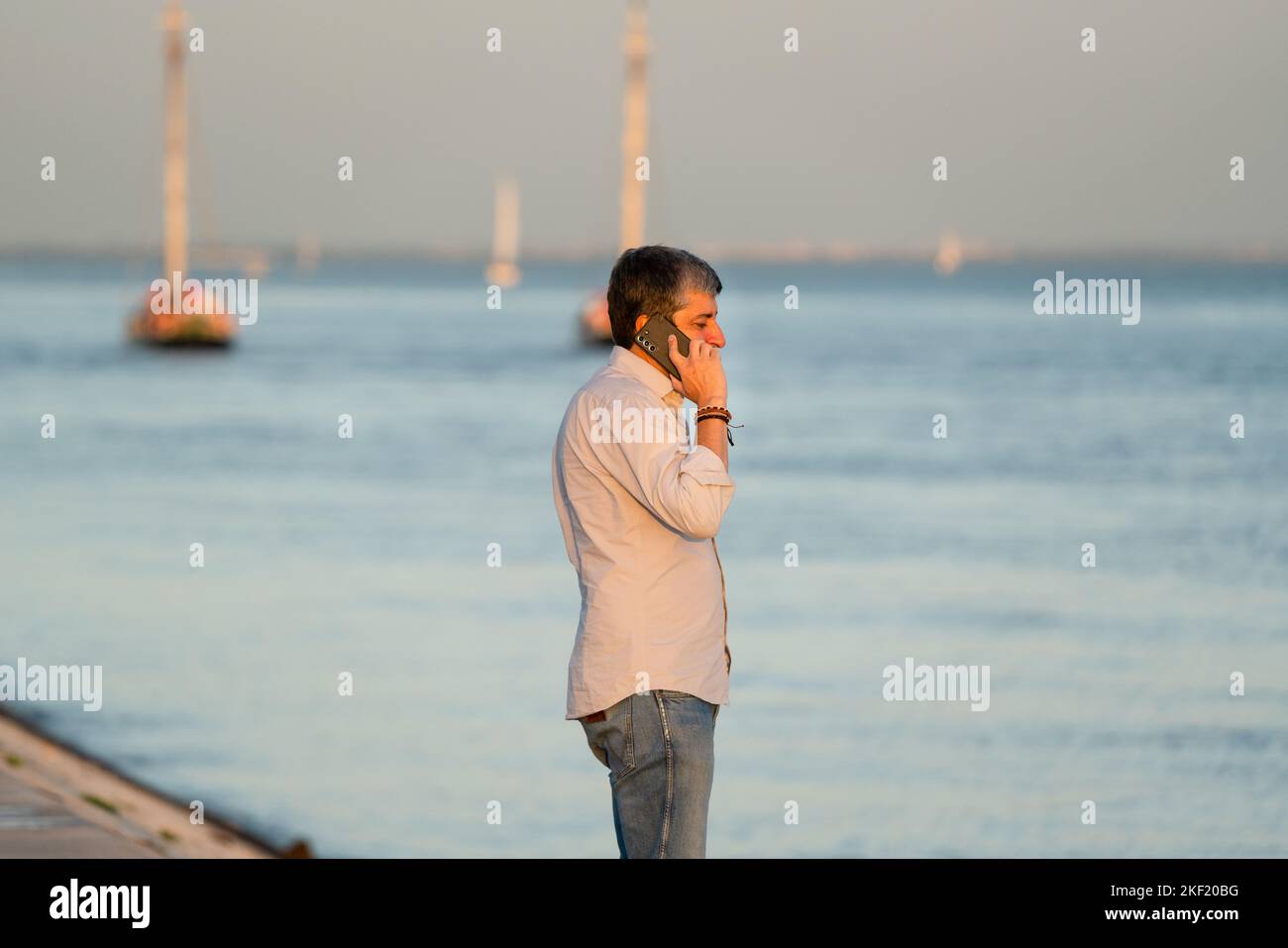 Un uomo sul suo cellulare al tramonto sulla Tejo Promenade il quartiere di Belem a Lisbona, Portogallo. Foto Stock