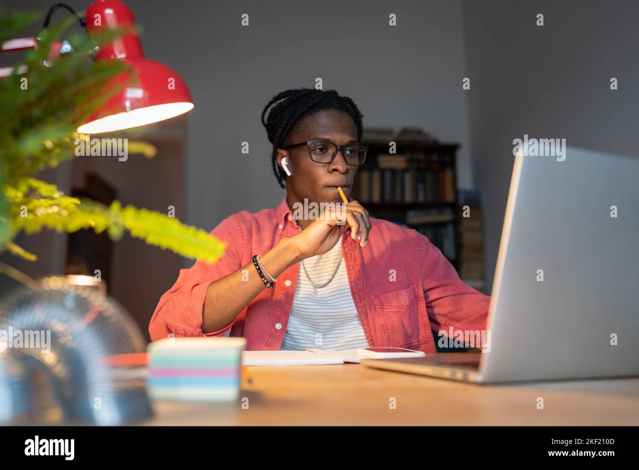 Un uomo afro-americano concentrato e penoso studentessa guarda il portatile seduto al computer in ufficio Foto Stock