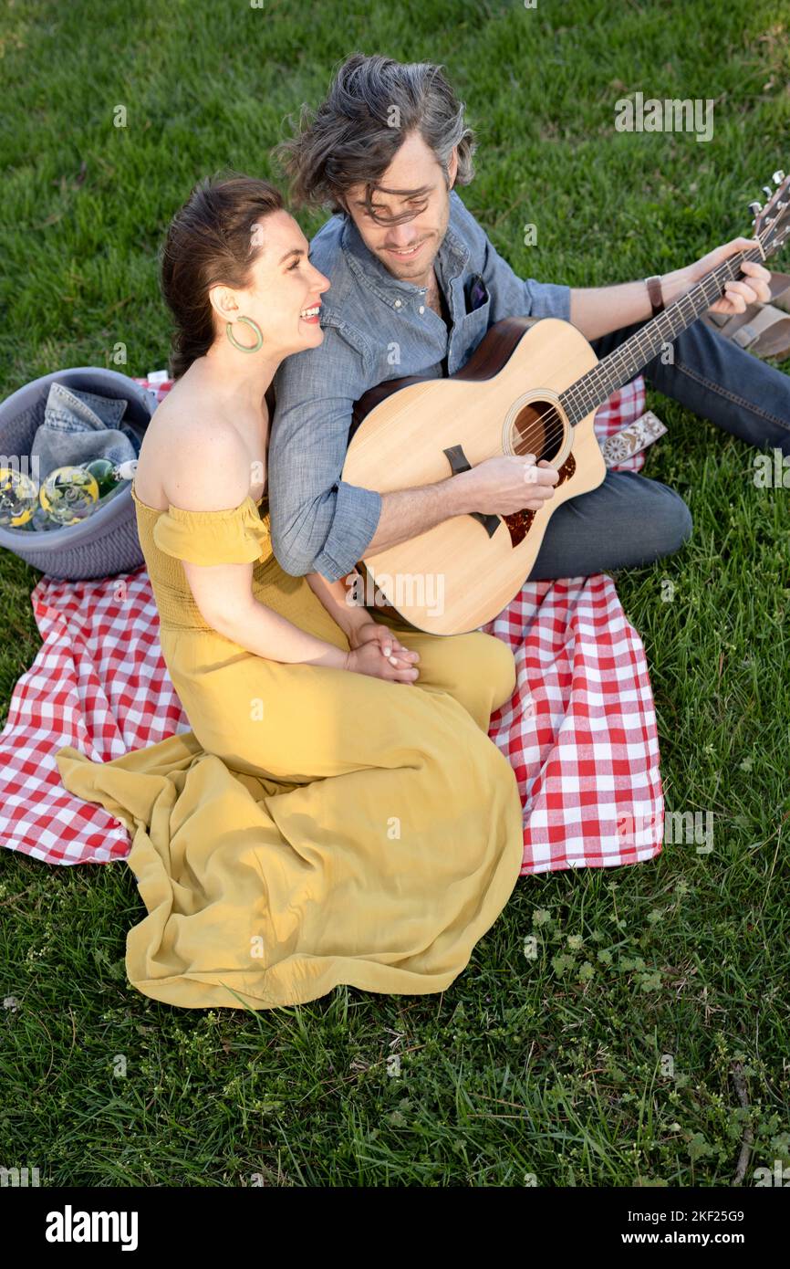 Coppia innamorata di un picnic nel Forest Park. L'uomo sta suonando una chitarra per la sua donna. Foto Stock