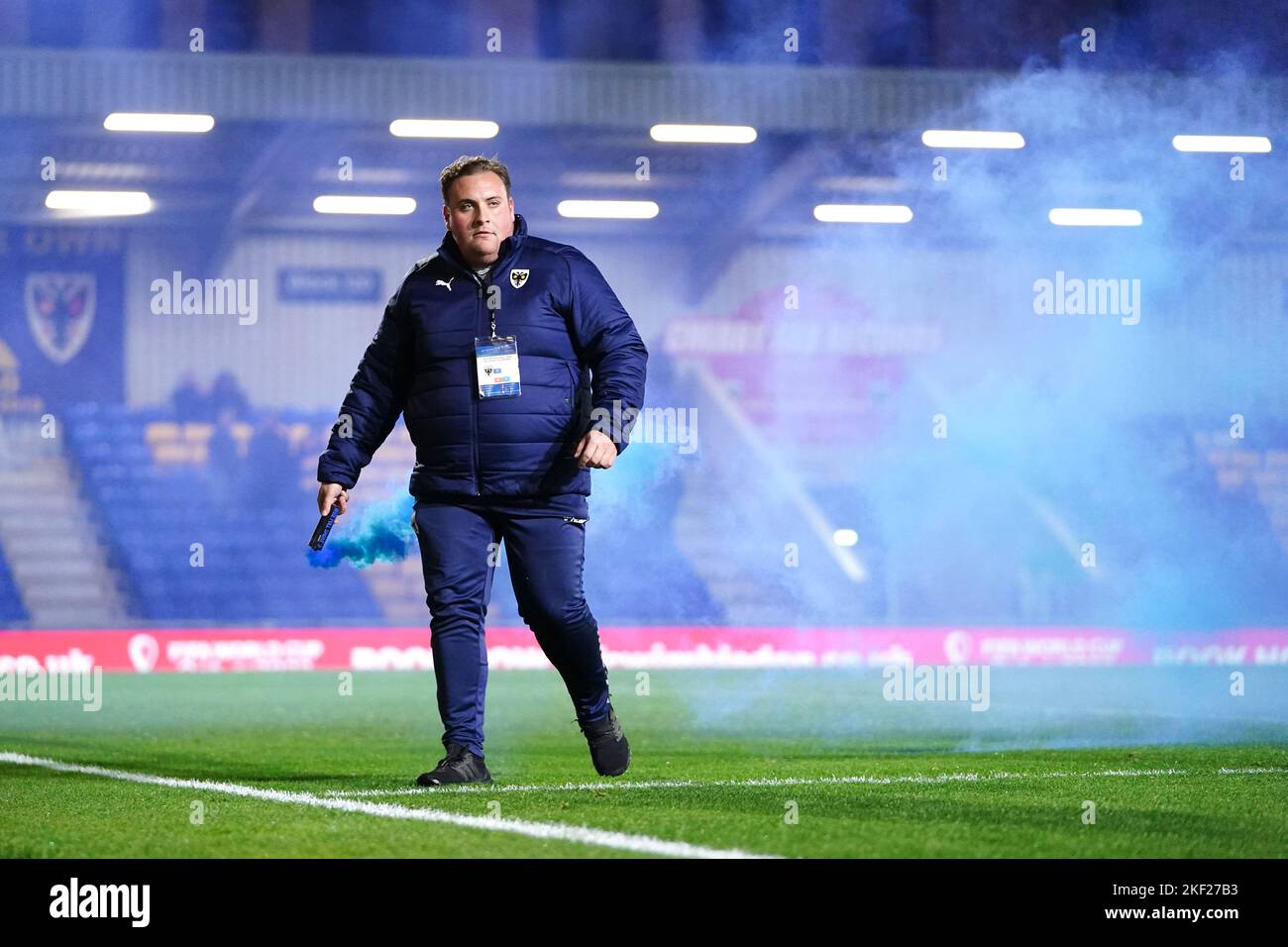 Un flare viene rimosso dal campo da un volontario del giorno della partita durante la partita di riproduzione del primo round della Emirates fa Cup al Cherry Red Records Stadium, Londra. Data immagine: Martedì 15 novembre 2022. Foto Stock