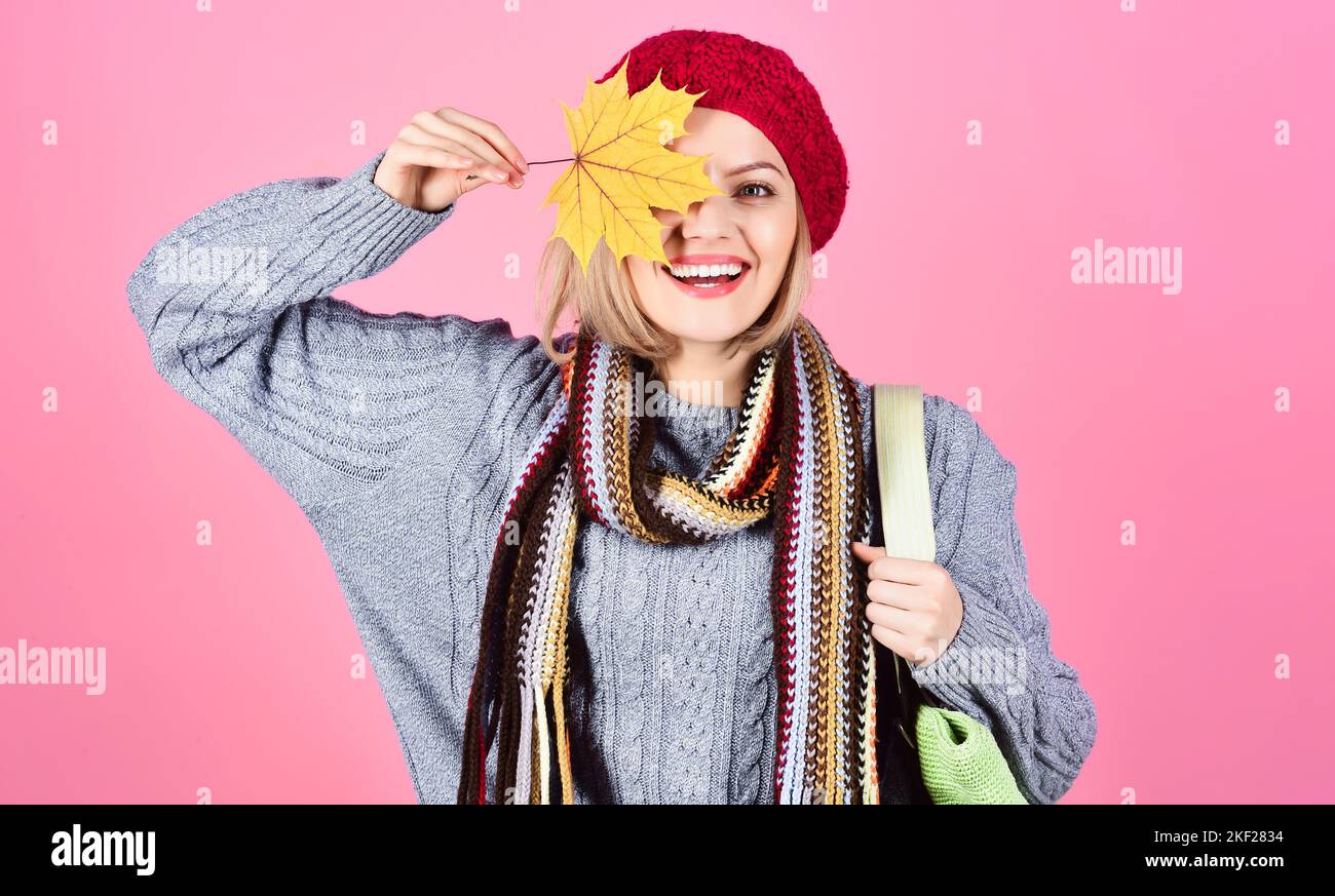 La ragazza sorridente nasconde l'occhio dalla foglia di acero giallo. Donna in abiti caldi con borsa per la spesa. Vendita stagionale. Foto Stock