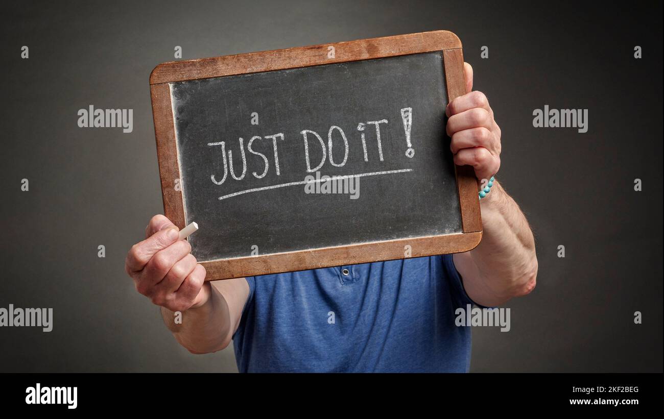 Frase motivazionale o appello per azione, appena lo faccia, manoscritto con il gesso bianco su una lavagna tenuta da una persona Foto Stock