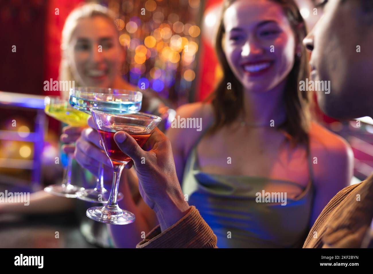 Tre amici maschi e femmine felici e diversi fanno un brindisi con cocktail in un bar nightclub Foto Stock