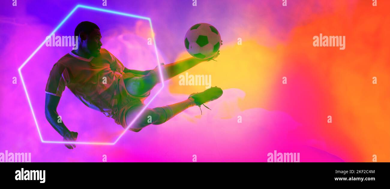Giocatore di calcio maschile afro-americano che salta e calcia palla da esagono su sfondo fumoso Foto Stock Giocatore di calcio maschile afro-americano che salta e calcia palla da esagono su sfondo fumoso Foto Stock