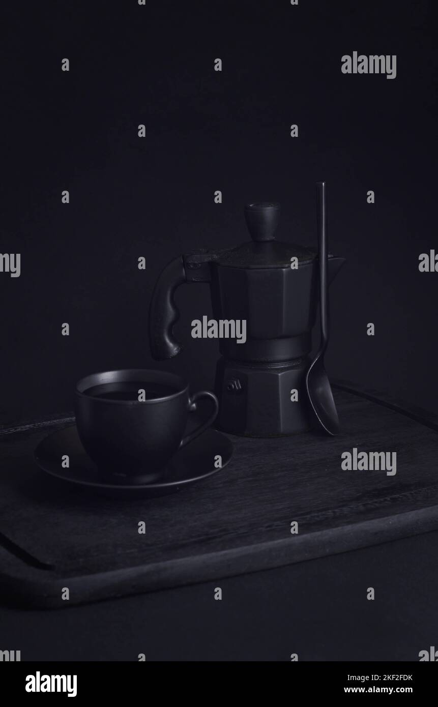Caffè italiano. Tazza di espresso caldo, moka pot su un asse di legno rustico, sfondo scuro, messa a fuoco selettiva. Natura morta, fotografia scura. Foto Stock
