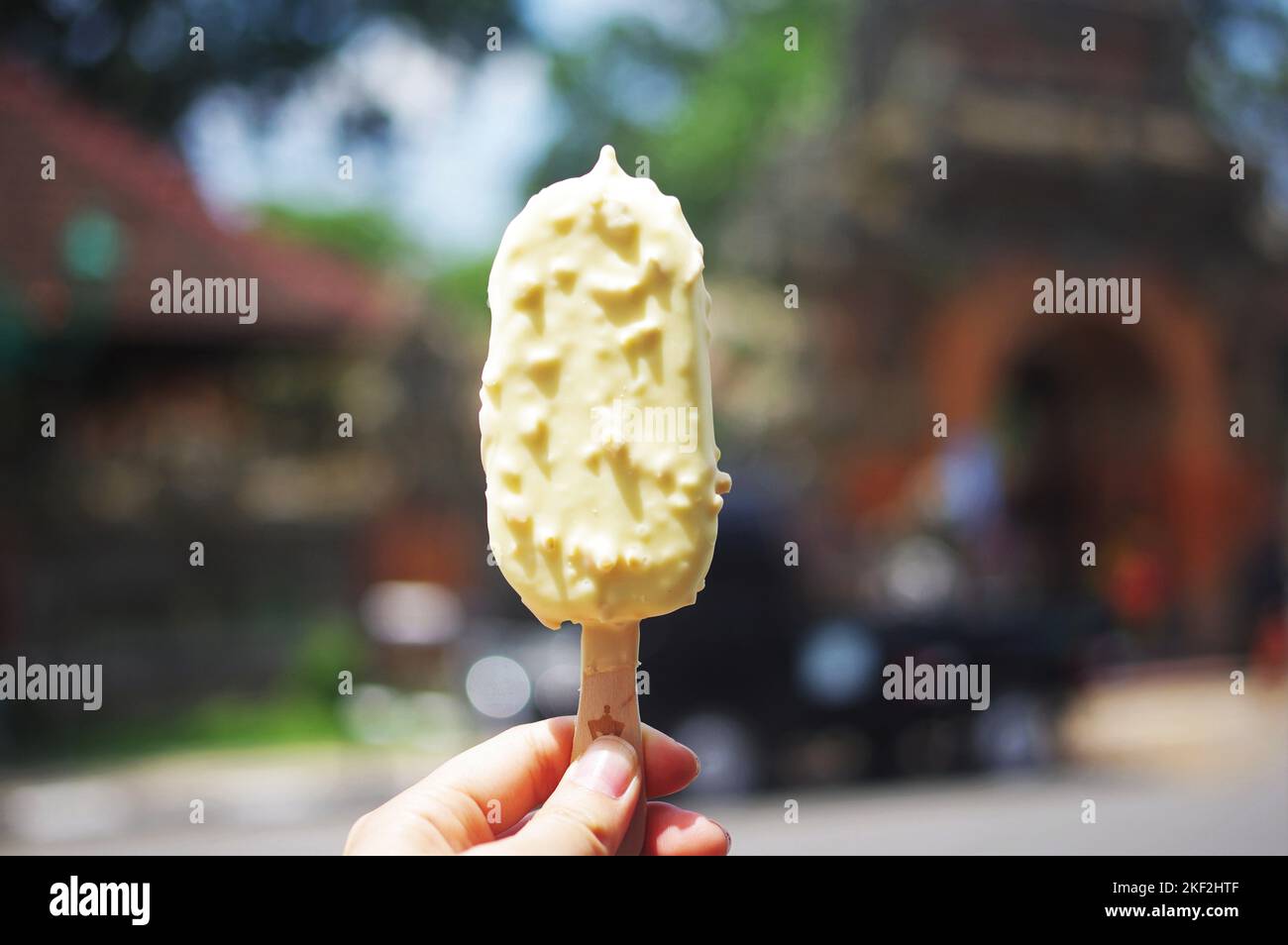 Mano che sorregge una gelateria al cioccolato bianco di fronte al Palazzo di Ubud in una calda giornata estiva: Bali, Indonesia Foto Stock