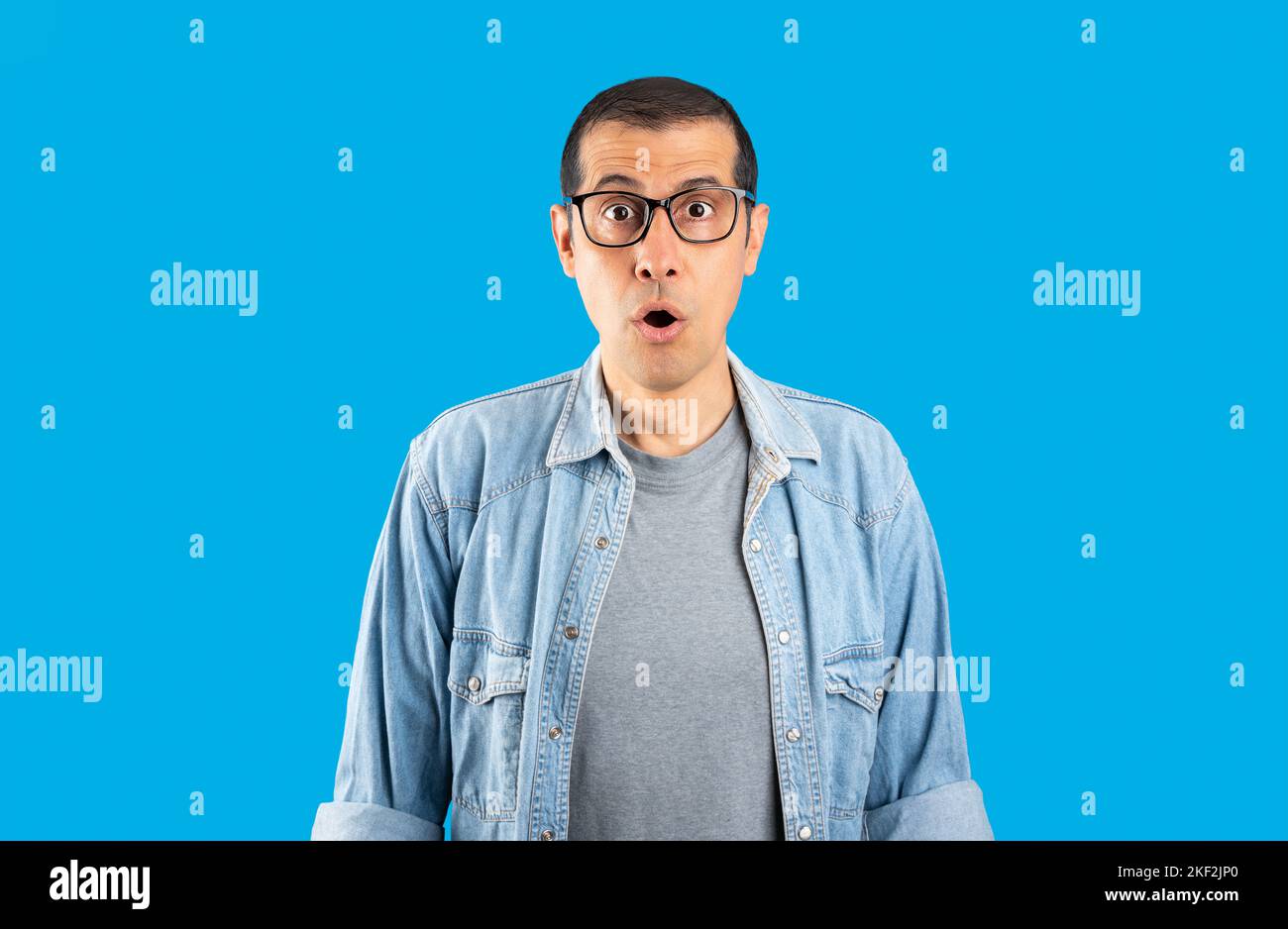 Studio shot di un uomo ispanico indossando occhiali sopra isolato sfondo blu paura e scioccato con sorpresa espressione, paura e viso eccitato. Foto Stock