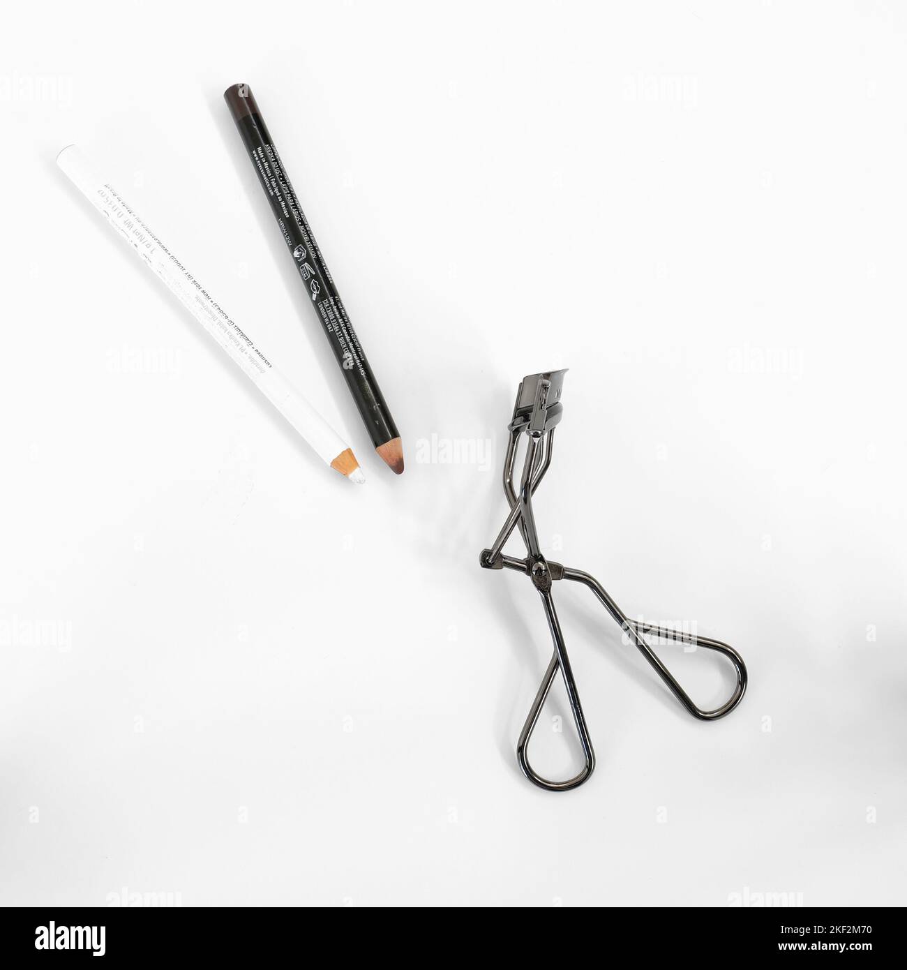Matita marrone, matita bianca e arricciacapelli con ciglia su sfondo bianco; trucco e cosmetici per labbra e occhi. Foto Stock