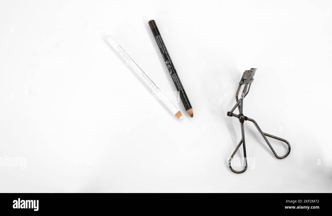 Matita marrone, matita bianca e arricciacapelli con ciglia su sfondo bianco; trucco e cosmetici per labbra e occhi. Foto Stock