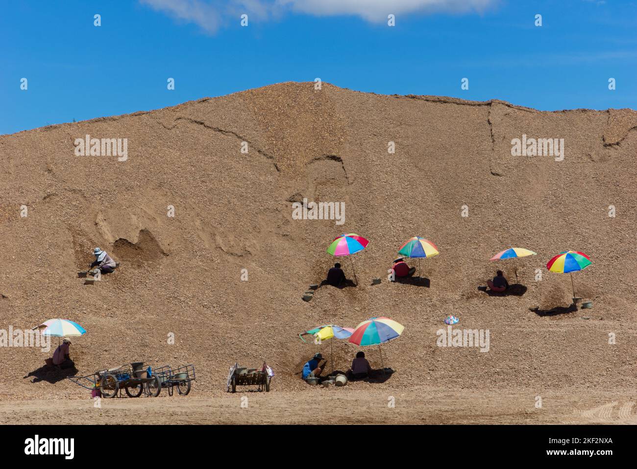 Persone thailandesi che lavorano insieme su un progetto in massiccia pila di sabbia con ombrelloni colorati e sfondo blu cielo. Foto Stock