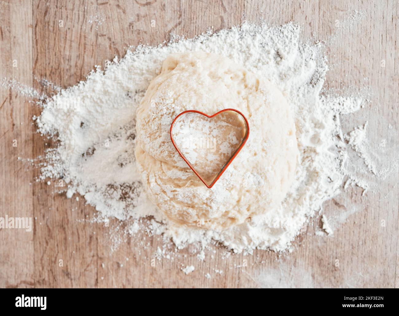 Farina da forno in cucina, tavola con struttura in legno e dessert da cucina con taglierina per biscotti al cuore. Pasta d'amore in pasta di torta di grano, ricetta per la cottura della pizza Foto Stock