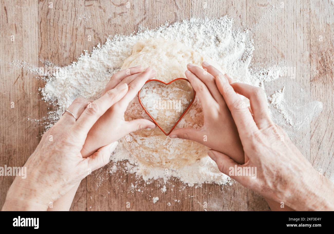 Mani, cottura e forma del cuore con una ragazza e nonna imparando come cuocere in cucina della loro casa insieme. Famiglia, bambini e cibo con Foto Stock