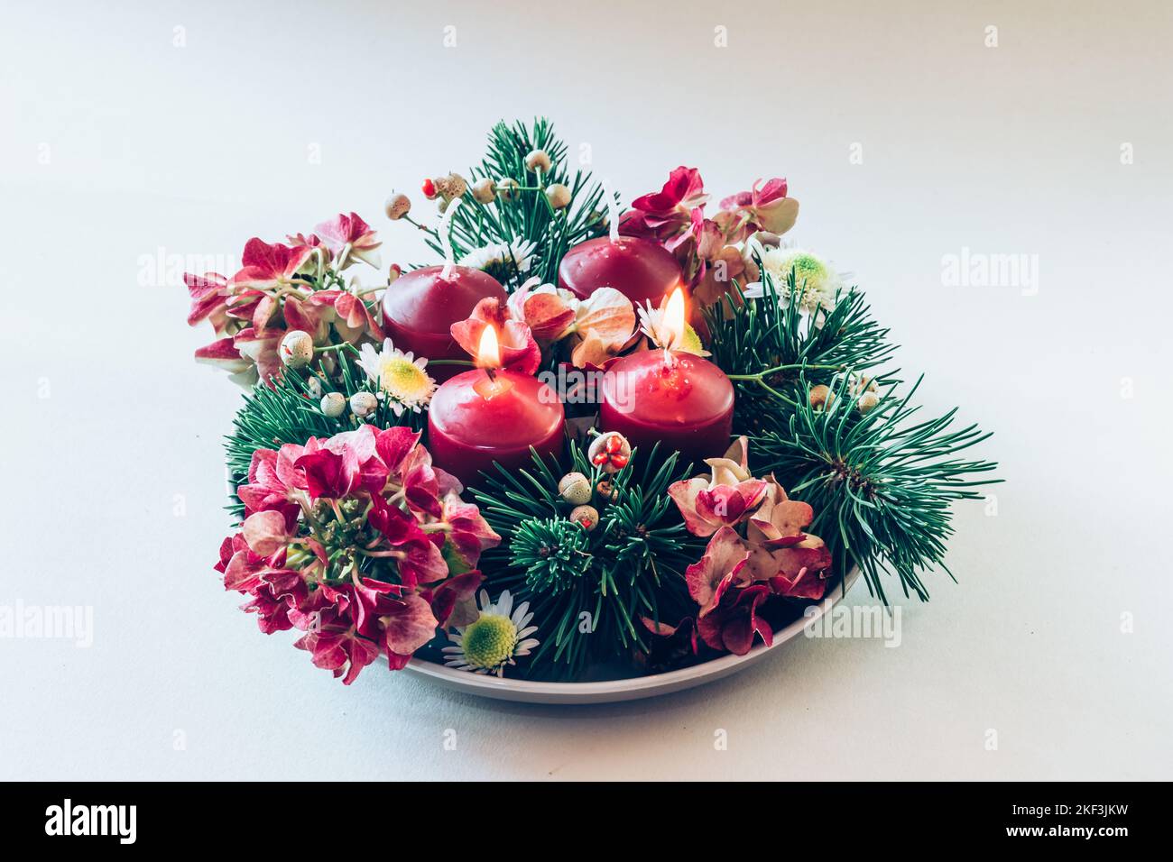 4 candele rosse d'avvento in corona cristiana religiosa tradizionale decorata con fiori di abete verde e ortensia Foto Stock