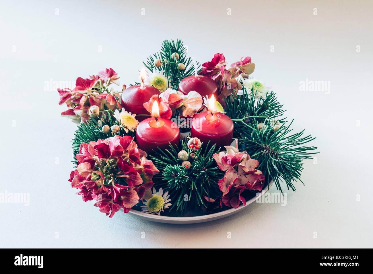 4 candele rosse d'avvento in corona cristiana religiosa tradizionale decorata con fiori di abete verde e ortensia Foto Stock