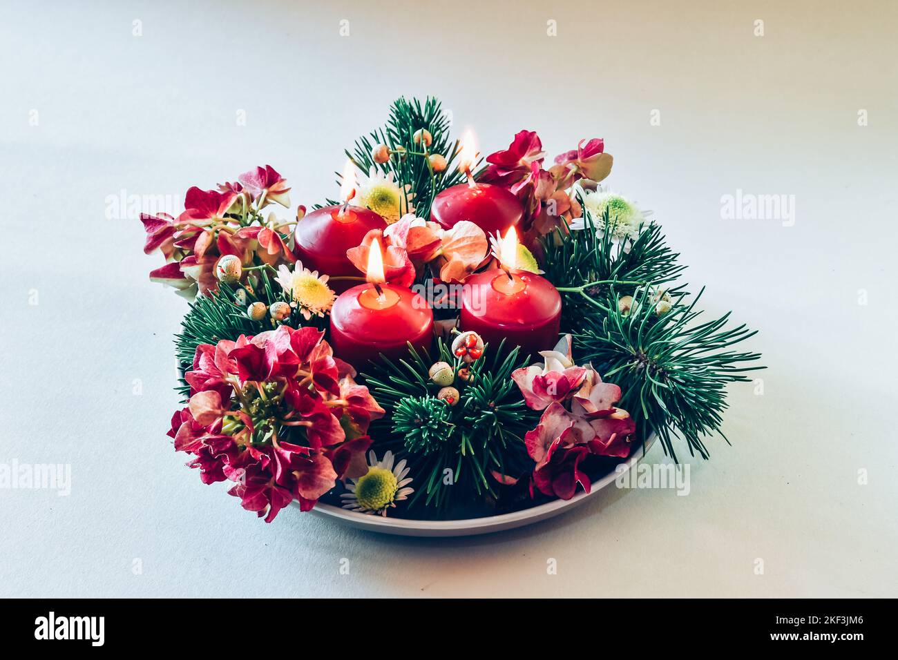 4 candele rosse d'avvento in corona cristiana religiosa tradizionale decorata con fiori di abete verde e ortensia Foto Stock