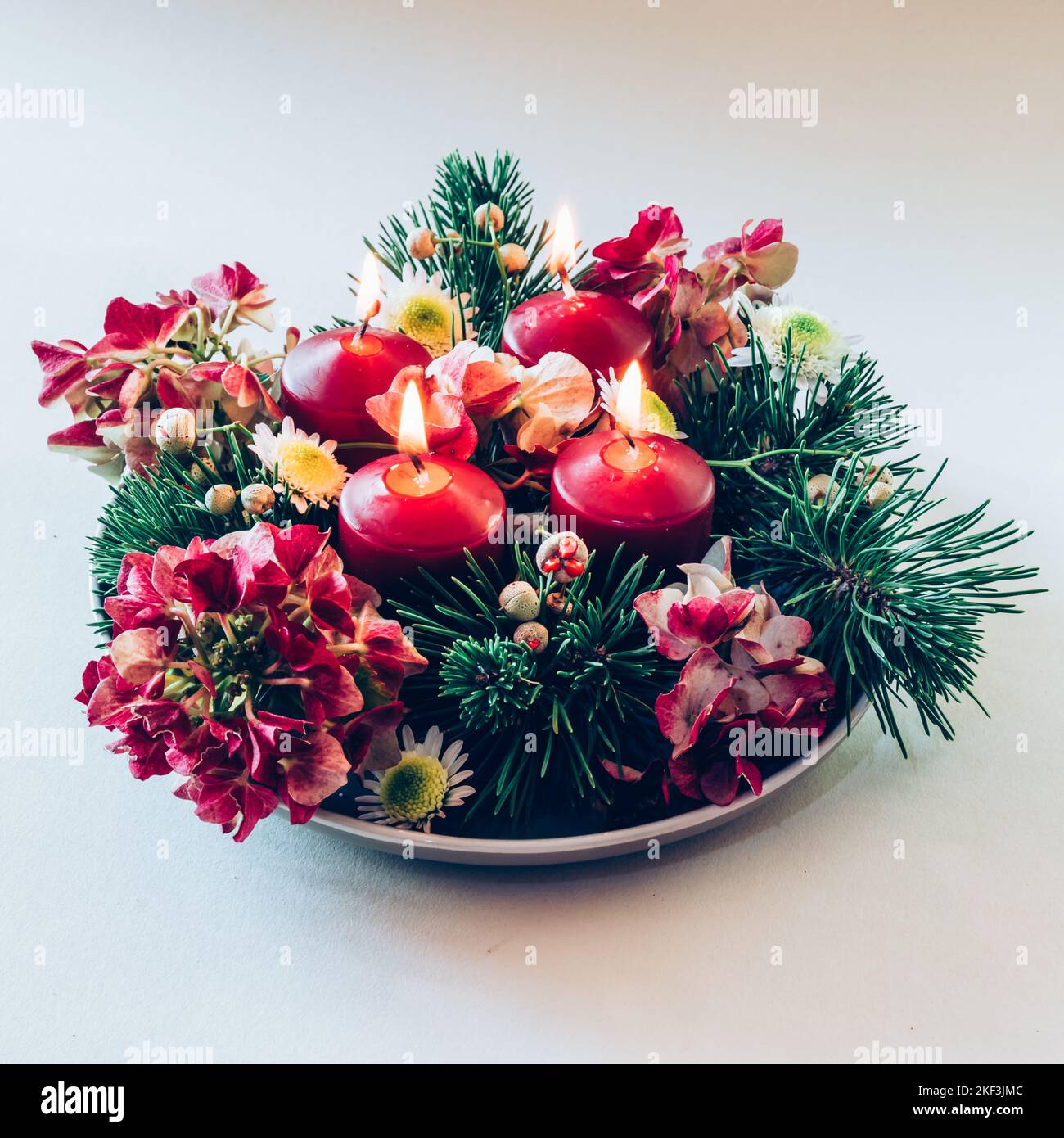 4 candele rosse d'avvento in corona cristiana religiosa tradizionale decorata con fiori di abete verde e ortensia Foto Stock