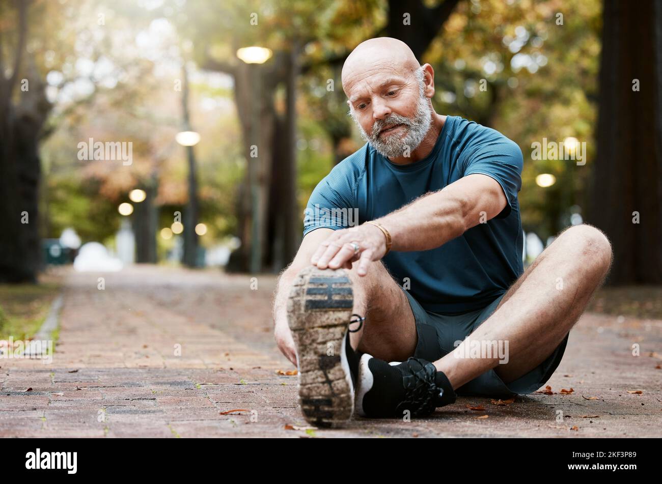 Fitness, esercizio fisico e stretching gambe uomo anziano in un parco all'aperto per l'energia, la salute e il benessere durante il pensionamento. Uomini anziani sani a terra Foto Stock