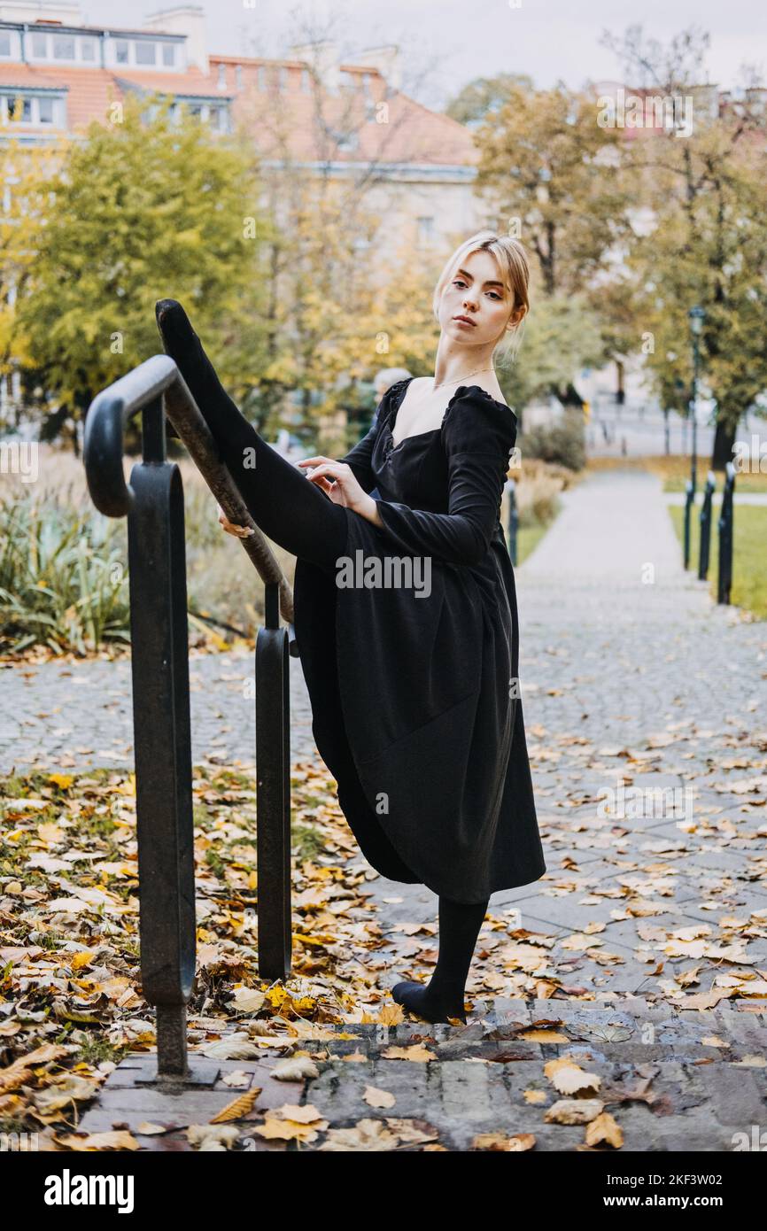 Ballerina Dancing in via autunnale città, ballerino moderno in vestito nero, Pointe Shoes Outdoors. Balsamo, balsamo quotidiano Foto Stock