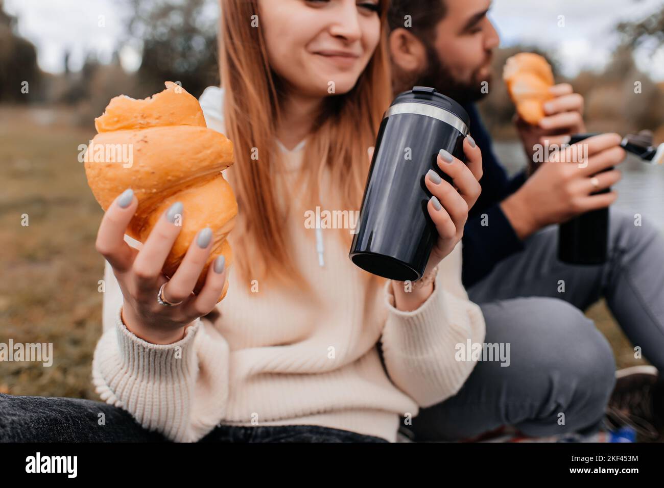 La coppia beve da una tazza termale e mangia croissant in una passeggiata nel parco. Foto Stock