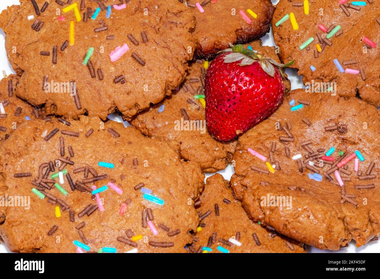 Vista ravvicinata della macrofotografia di biscotti al cioccolato fatti in casa con patatine colorate e una fragola. Direttamente sopra la vista macro. Foto Stock