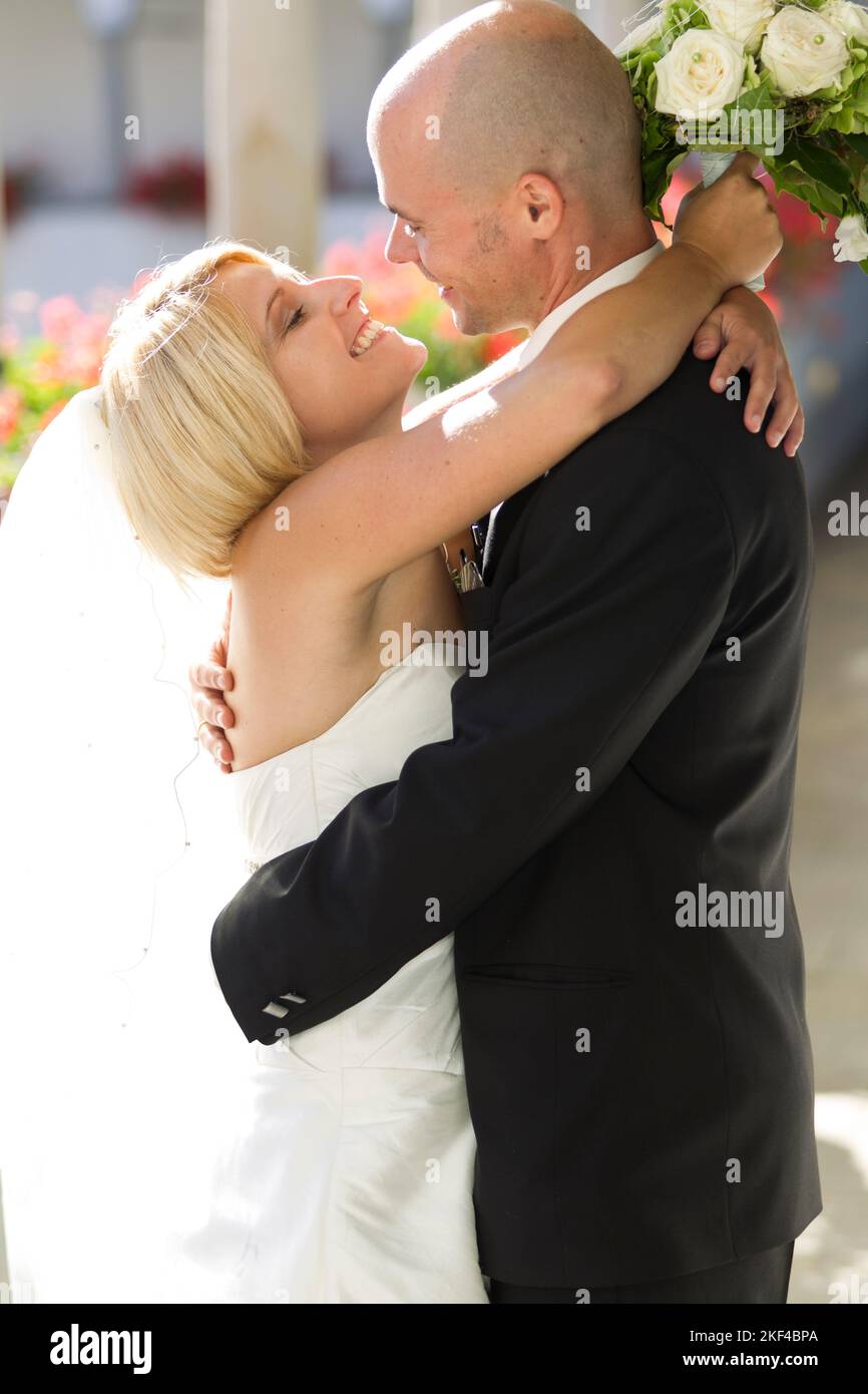 Eine glückliche Braut umarmt ihren frisch angetrauten Ehemann, 30, 35, Jahre, Blond, Blonde, Blondine, weisses Hochzeitskleid, Anzugträger, Foto Stock