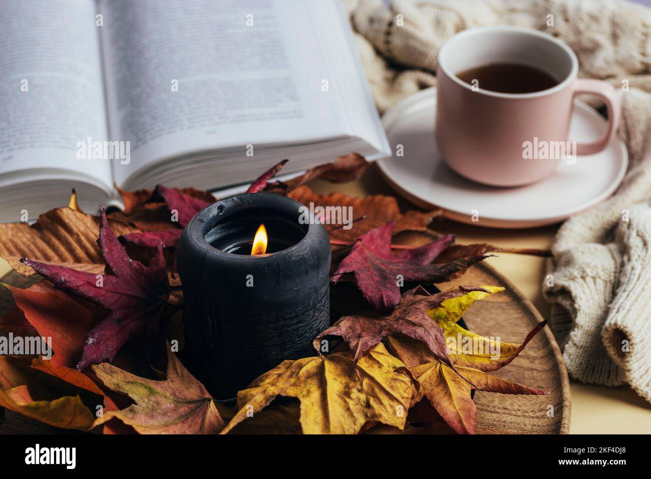 Candela bruciante decorata con foglie autunnali, libro aperto e caffè in tazza su un tavolo. Casa accogliente, concetto autunnale. Messa a fuoco selettiva. Foto Stock
