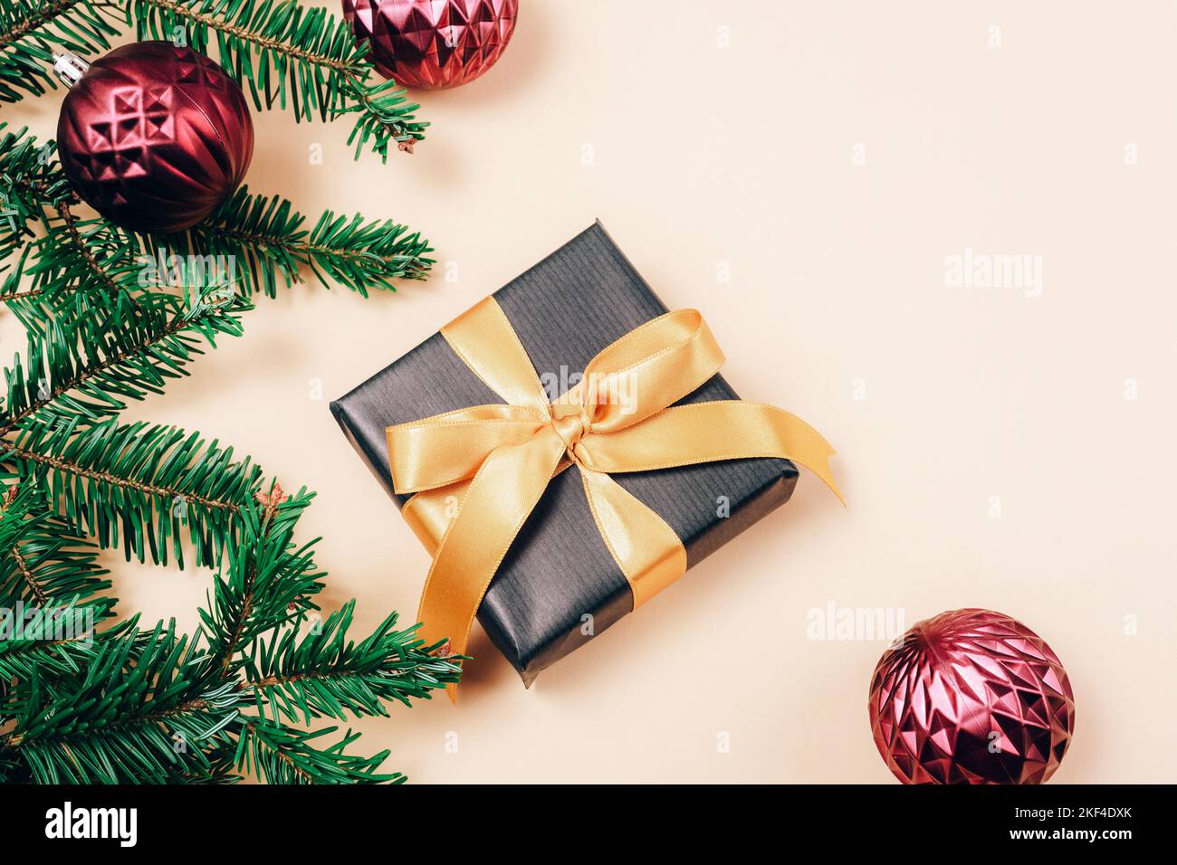 Scatola regalo e rami di abete con decorazioni natalizie su sfondo beige. Concetto di vacanza invernale. Vista dall'alto, disposizione piatta, spazio di copia. Foto Stock