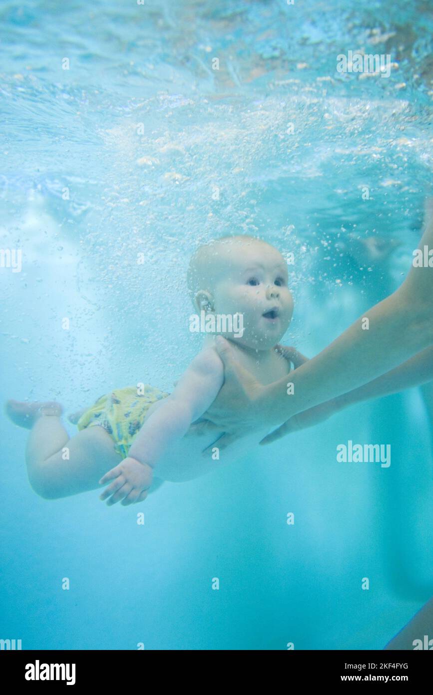 Baby schwimmt unter Wasser mit offenen Augen, gestützt von den Armen der Mutter, Babyschwimmen, Säugling, 6 Monate, Schwimmbad, Foto Stock