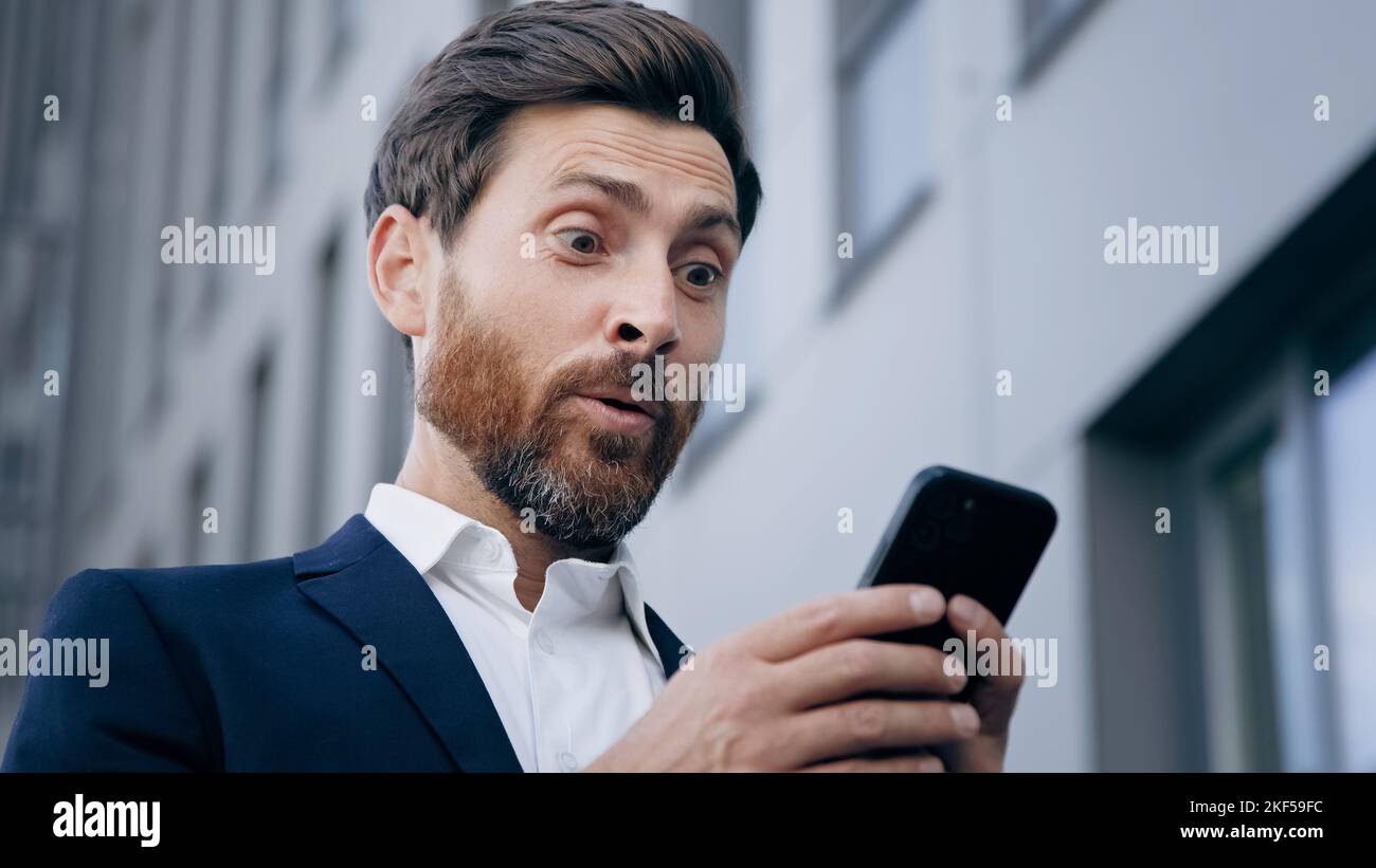 Primo piano giovane uomo sorpreso guarda lo schermo del telefono che riceve la notifica lettura buona notizia gioire nel successo uomo d'affari soddisfatto ottiene eccellente Foto Stock