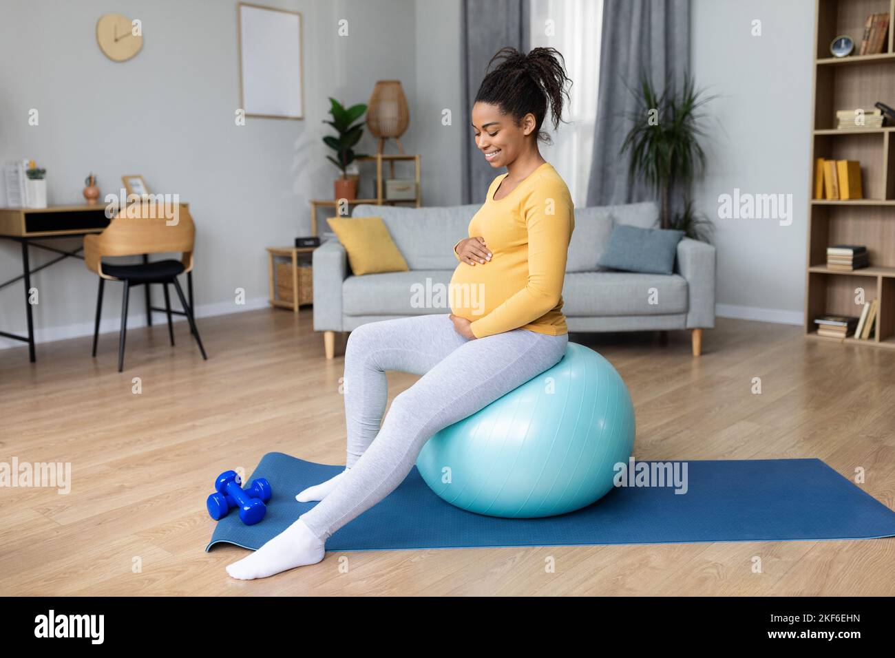 Sorridente giovane donna nera incinta con pancia grande fare esercizi sulla palla fitness e si sente movimenti del bambino Foto Stock