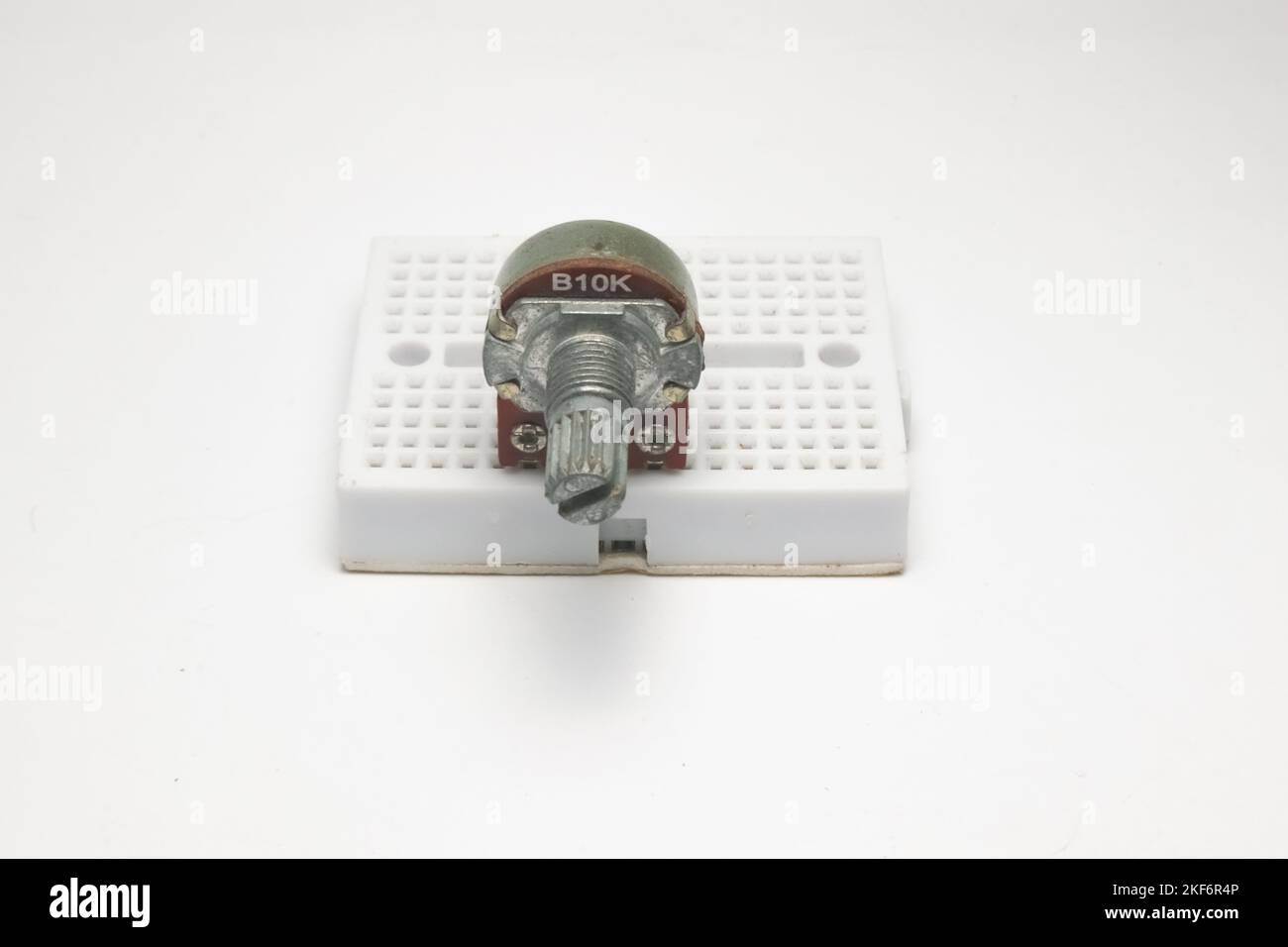 Un resistore variabile o potenziometro con codice B10K si attacca a una piccola vista frontale della scheda di progetto su sfondo bianco. Foto Stock