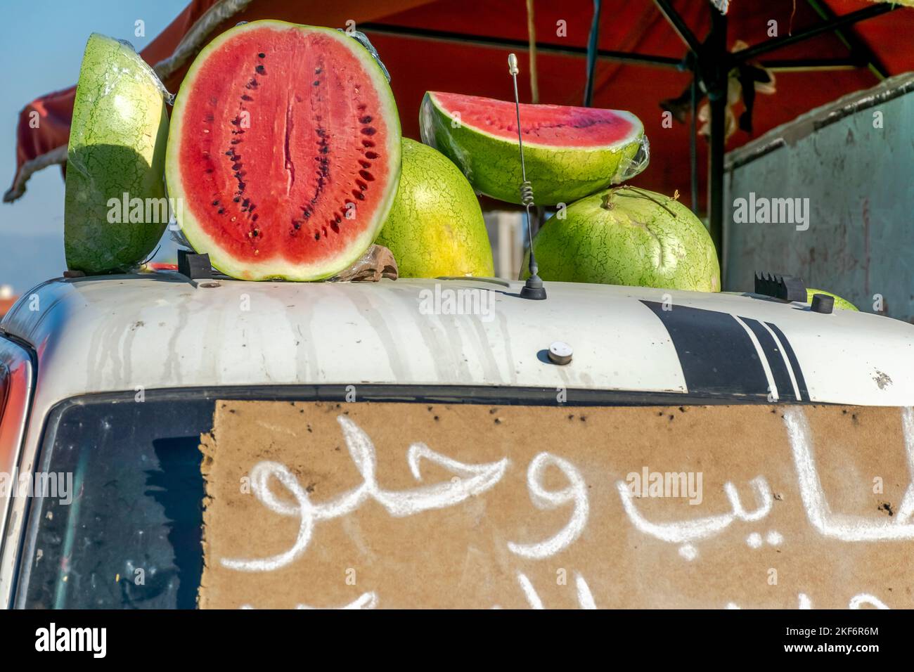 Molti cocomeri in vendita. Chiuso e mezzo aperto e accatastato su casse. Esposto su un mini-camion con un'iscrizione a mano in gesso arabo. Foto Stock