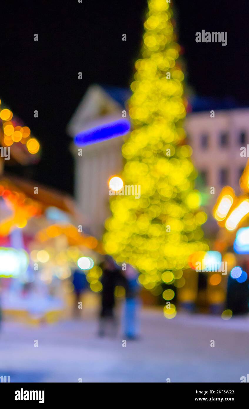 Sfondo sfocato. Albero di Natale, luci decorate, edificio, sagome sfocate di persone che camminano piazza della città durante la notte d'inverno. Bello Capodanno e Natale vacanza sfondo sfocato Foto Stock