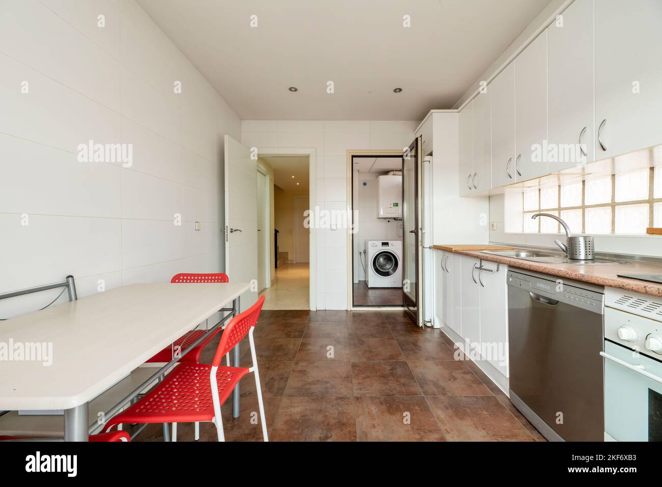 Cucina con armadi in legno bianco, elettrodomestici da incasso e cucina da pranzo con sedie rosse Foto Stock