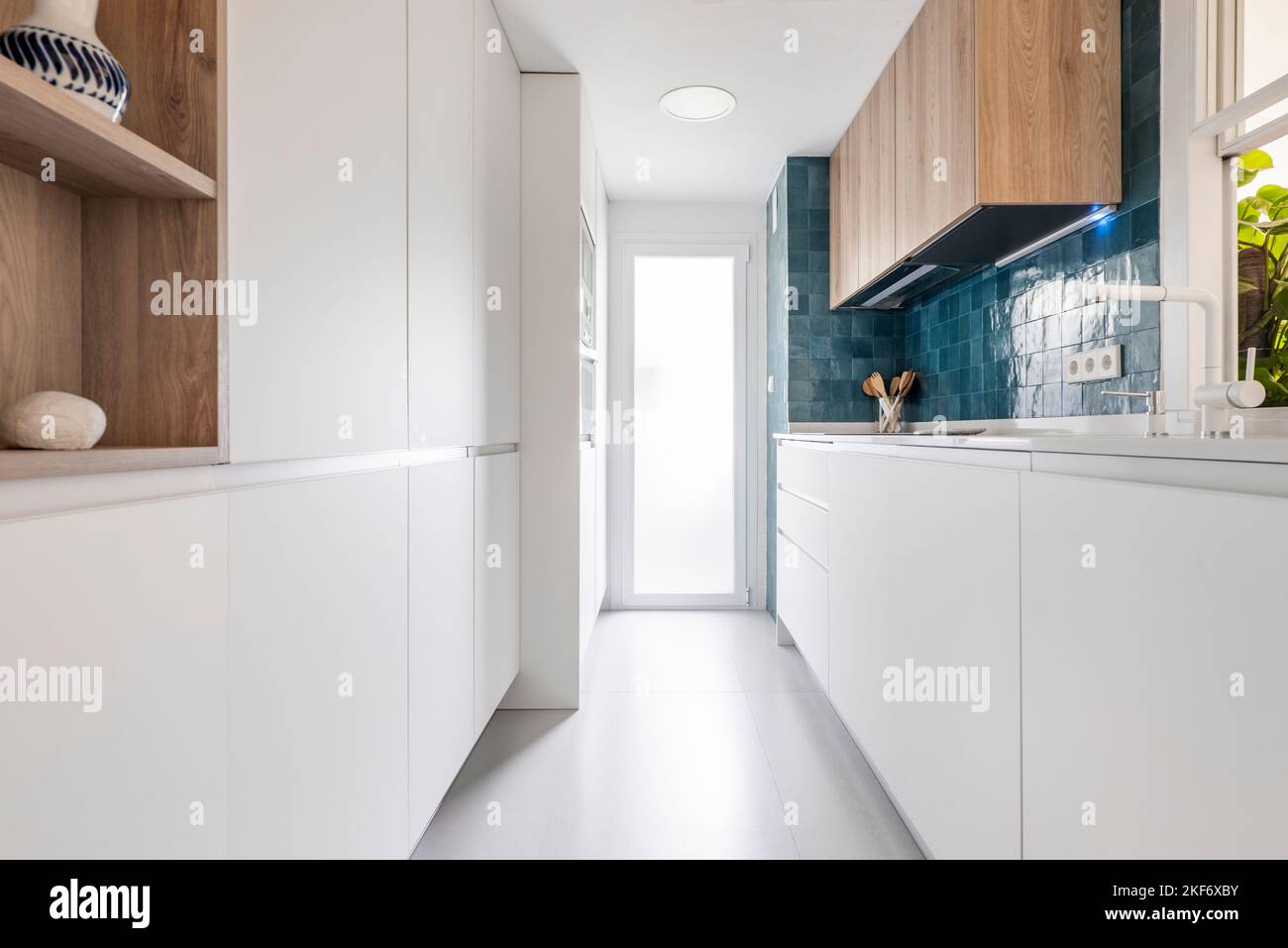 Cucina con armadi in legno bianco senza maniglie e parete blu cobalto brillante Foto Stock