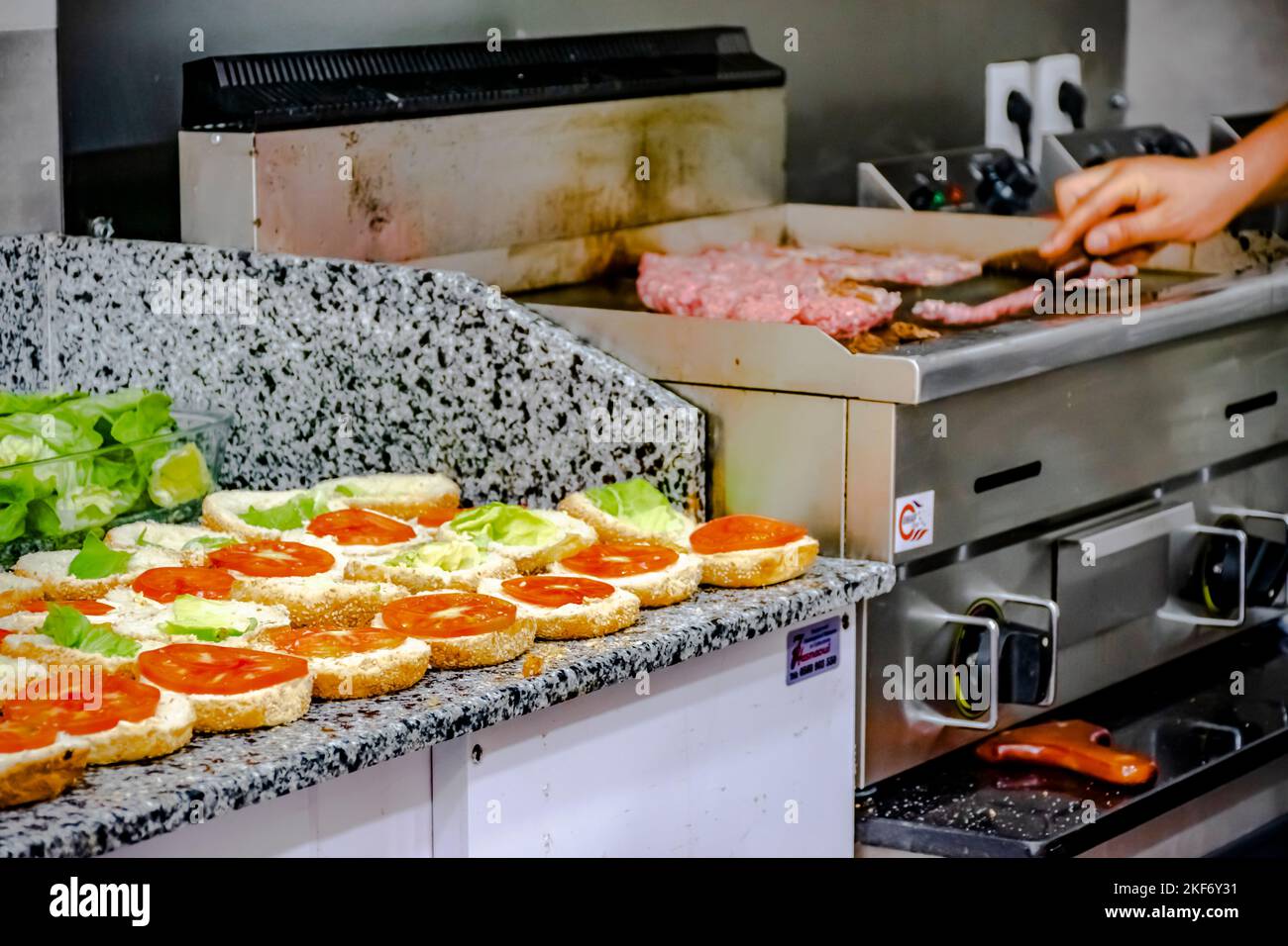 Babaarroudj Burgers in Dely Ibrahim. Hamburger aperti in fila con insalata di lattuga e pomodoro. Sfondo sfocato della cottura a mano del cuoco bistecca fresca tritata Foto Stock