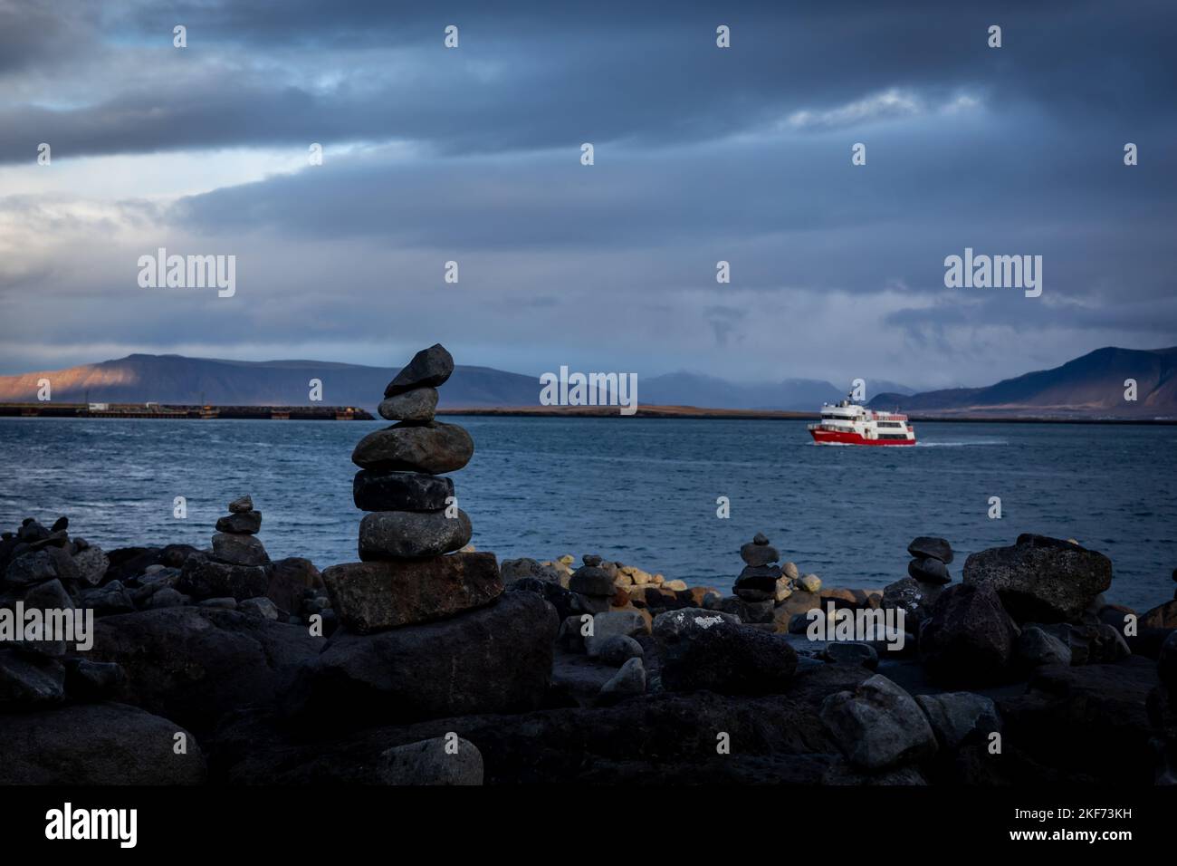 Reykjavik, Islanda - 10 novembre 2022: Barca turistica rossa che naviga verso il porto. Paesaggio sul mare, mucchi di roccia vulcanica in primo piano. Foto Stock