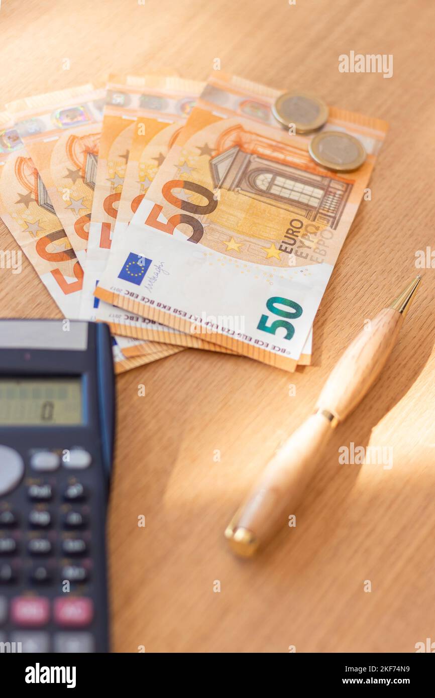 Vista verticale del borra di una cinquantina di euro e monete accanto a una calcolatrice e a una penna sopra un tavolo di legno con raggi solari Foto Stock