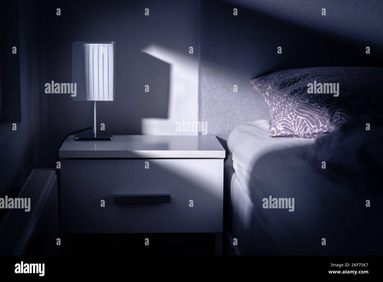 Luce di luna nella camera da letto di notte dalla finestra. Letto e tavolo in camera buia al tramonto. Design degli interni in moderno appartamento bianco. Luce blu dalla luna. Foto Stock