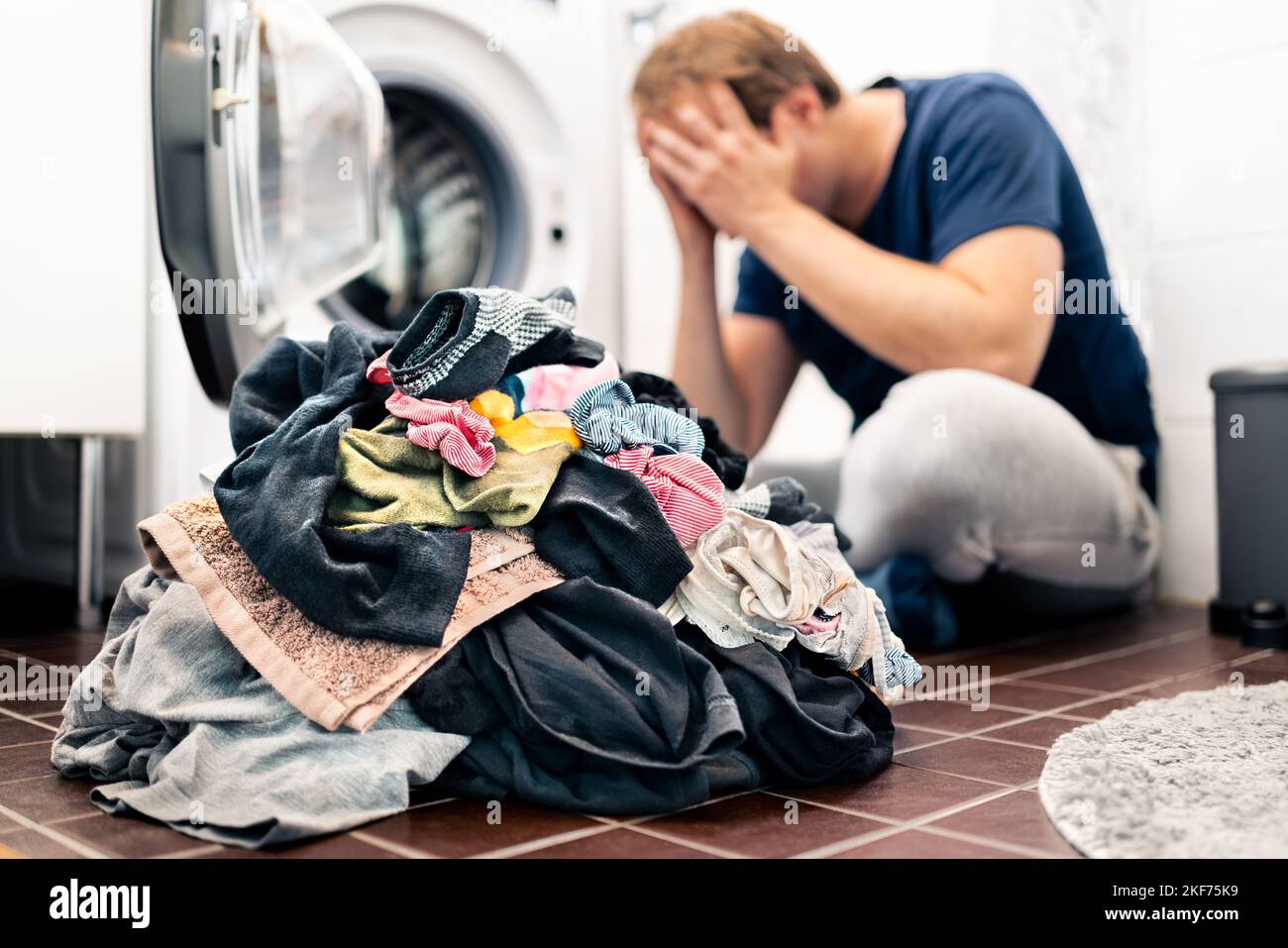 Stanco e infelice di bucato, vestiti di lavaggio, faccende domestiche e lavori di casa. Uomo triste o giovane papà sopraffatto. Lavatrice rotta. Stress genitorialità. Foto Stock