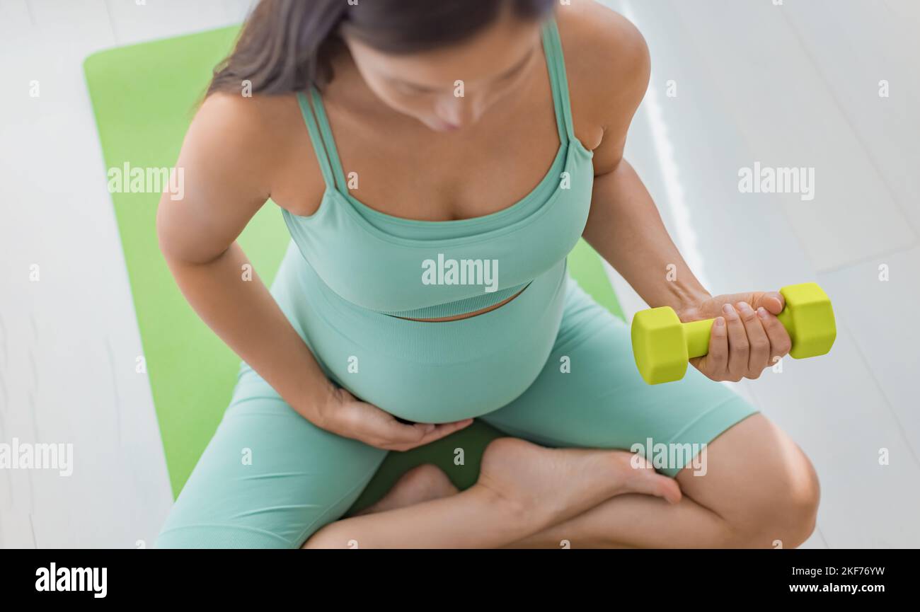 Gravidanza e concetto di esercizio fisico. Donna incinta allenamento a casa. Esercizio di allenamento per la forza fitness con pesi a manubri. Il braccio per l'allenamento del corpo ricci il primo piano Foto Stock