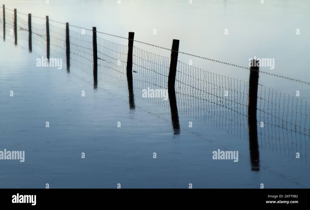 Riflessione di Un filo Fence in acque calme in Una tranquilla mattina Misty, Keyhaven UK Foto Stock