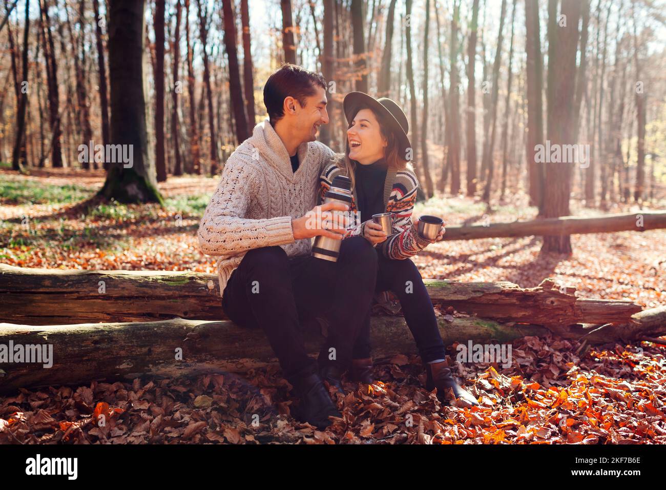 Ritratto di giovane coppia amorevole bere il tè da thermos relax nella foresta autunnale. L'uomo e la donna si siedono sul tronco ridendo Foto Stock