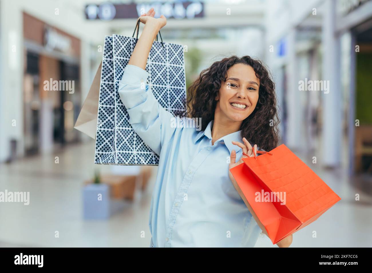 Vendita vacanze. Black Friday. Felice giovane donna ispanica shopping in un supermercato. Tiene in mano borse colorate per la spesa, le solleva, si rallegra, sorride alla fotocamera. Foto Stock