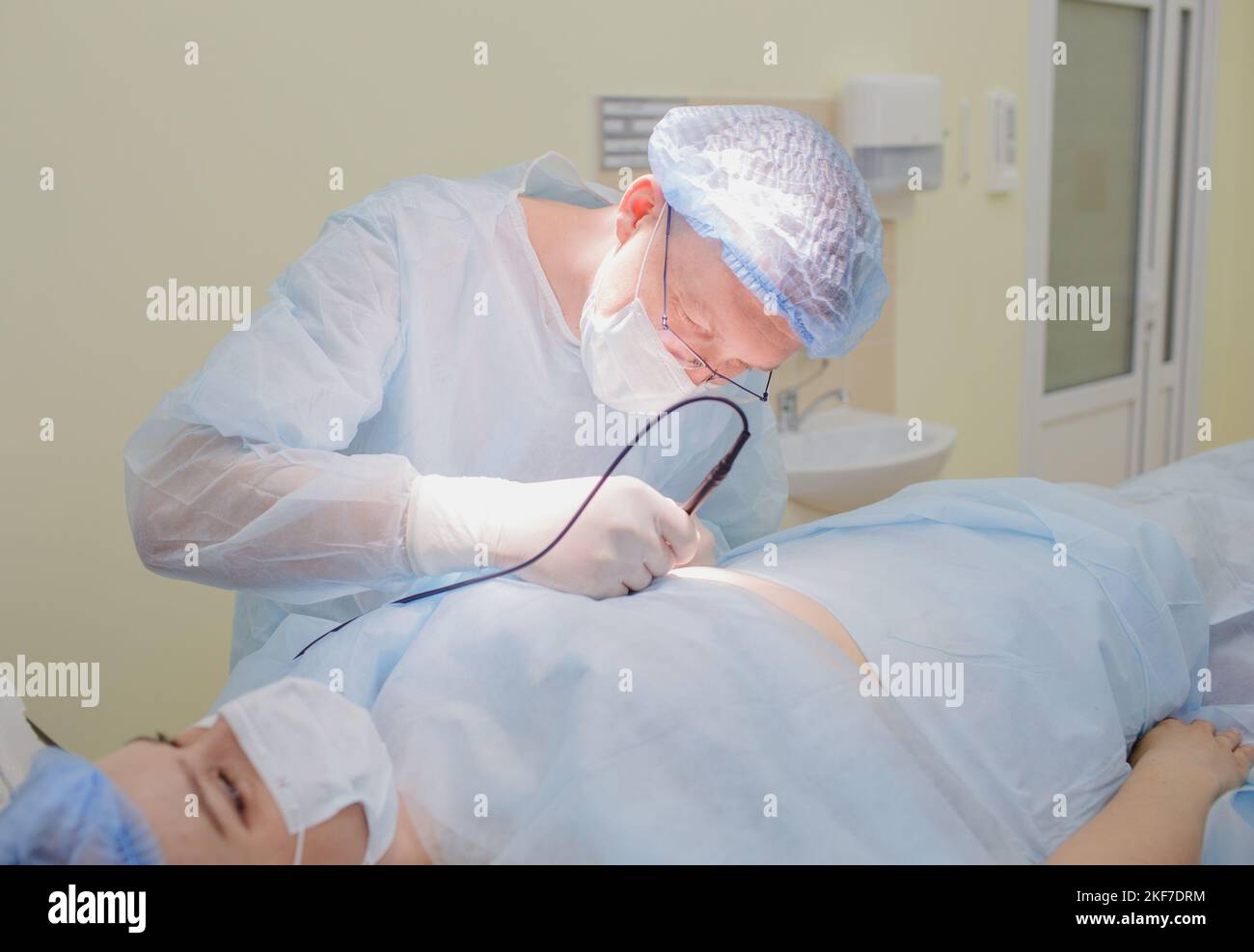 un chirurgo esperto esegue l'operazione sotto una lampada elettrica luminosa in una moderna sala operatoria. Foto Stock