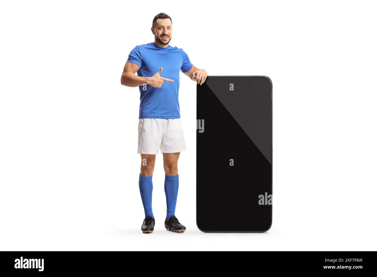 Ritratto completo di un giocatore di calcio che si trova accanto a un grande smartphone e che punta sullo schermo isolato su sfondo bianco Foto Stock Ritratto completo di un giocatore di calcio che si trova accanto a un grande smartphone e che punta sullo schermo isolato su sfondo bianco Foto Stock