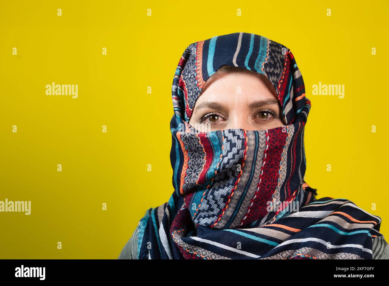 Primo piano ritratto di donna che indossa hijab, guardando la macchina fotografica, isolato su sfondo giallo studio. Foto Stock